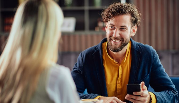 A man holding his phone sitting across a woman and smiling at her.